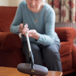 Senior Woman Using Reaching Arm To Pick Up Spectacles Case At Home