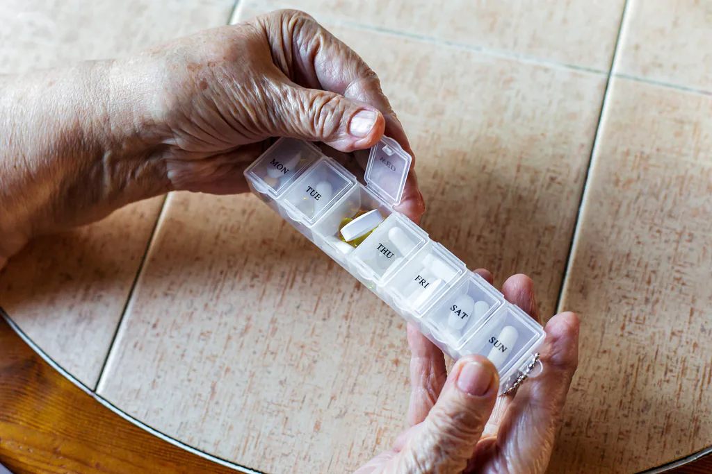 Close up senior woman hands holding weekly pill organizer with tablets sorted by days